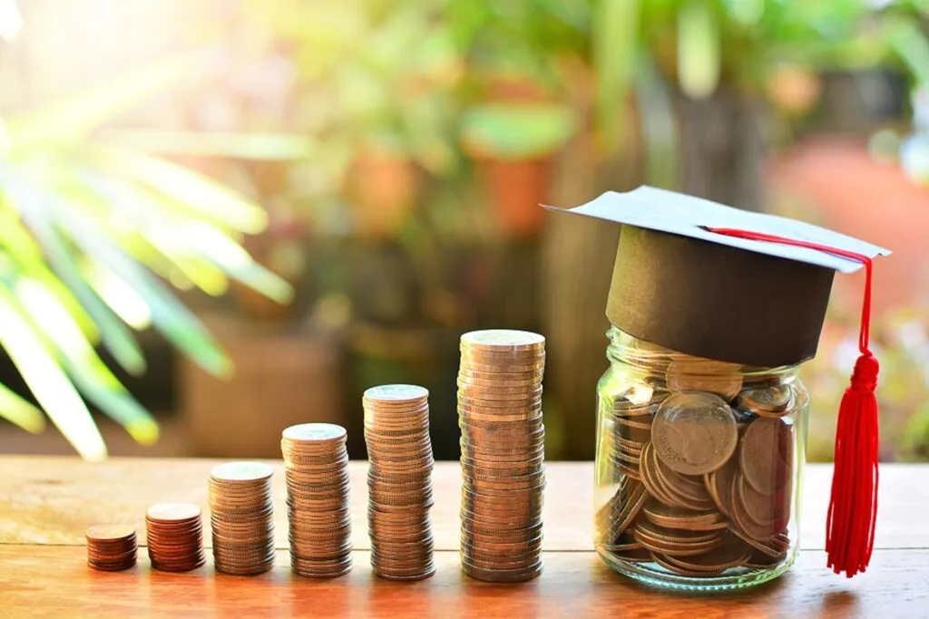 Piles of coins, coins in a jar, and a mini graduating hat