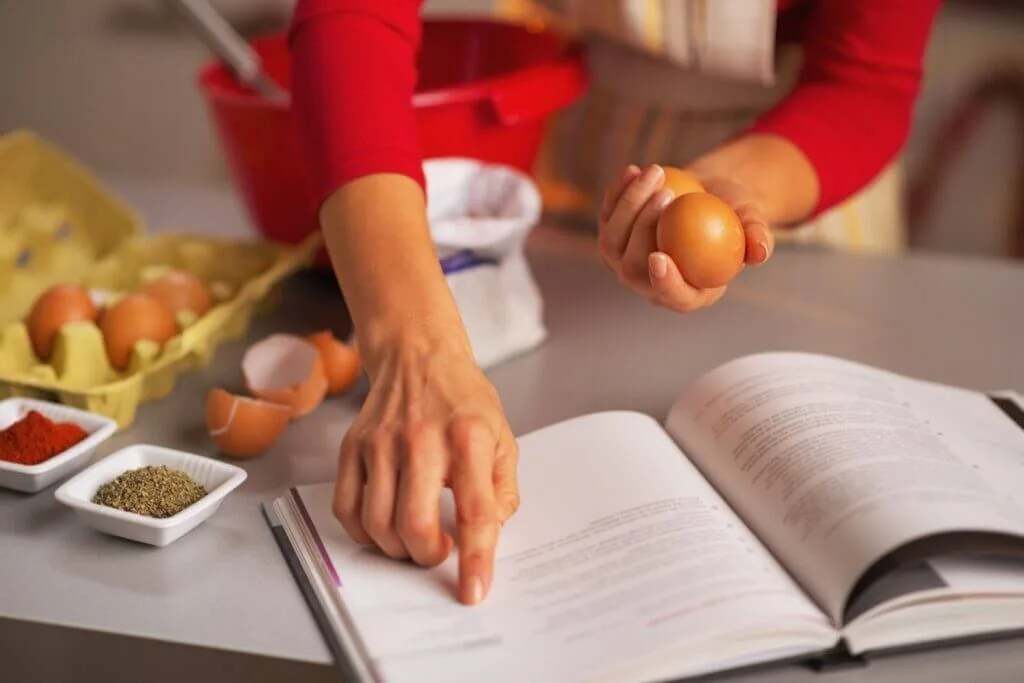 University student following a baking recipe, holding an egg in one hand.