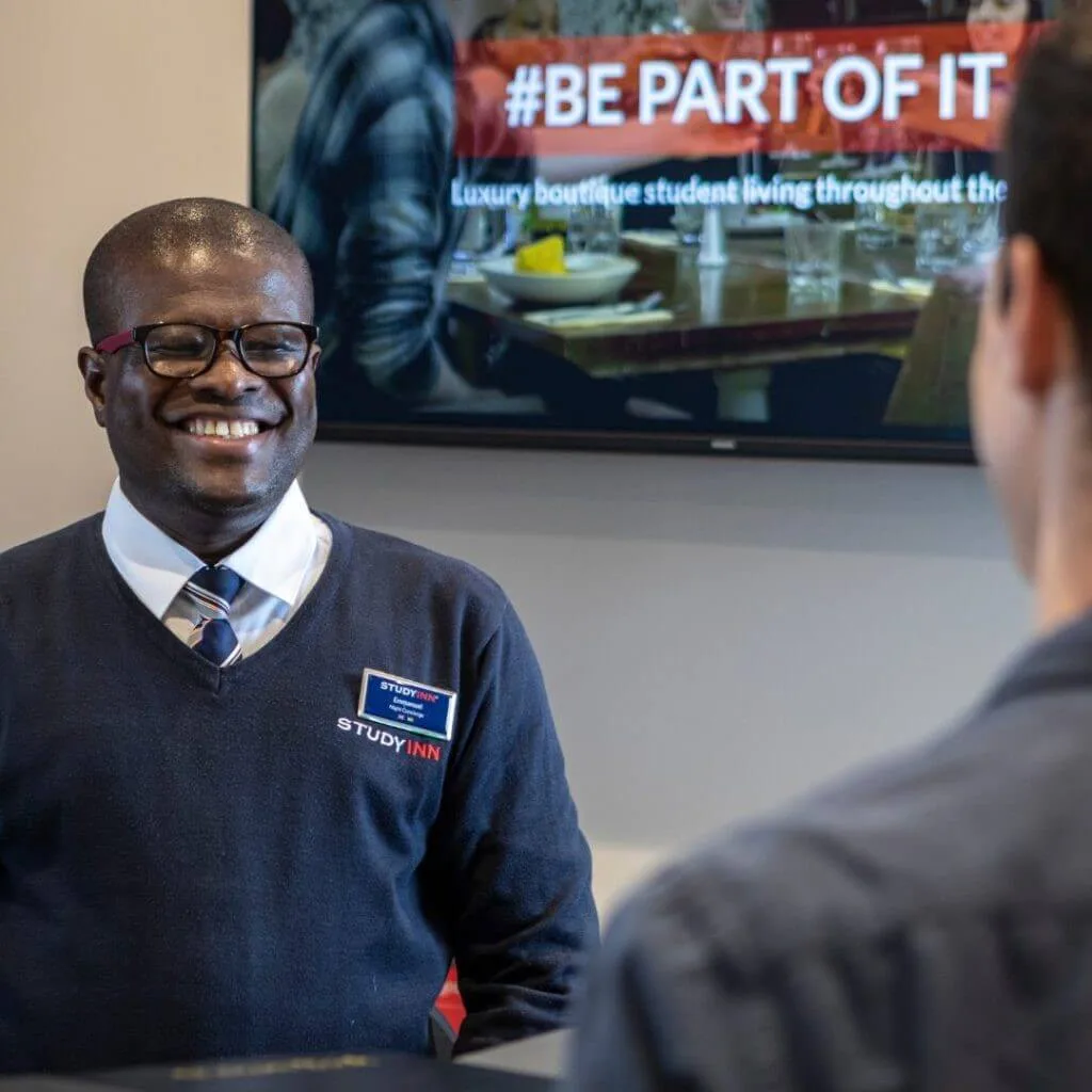Study Inn's security standing in front of a TV at reception smiling to a resident student at one of Study Inn student accommodations.