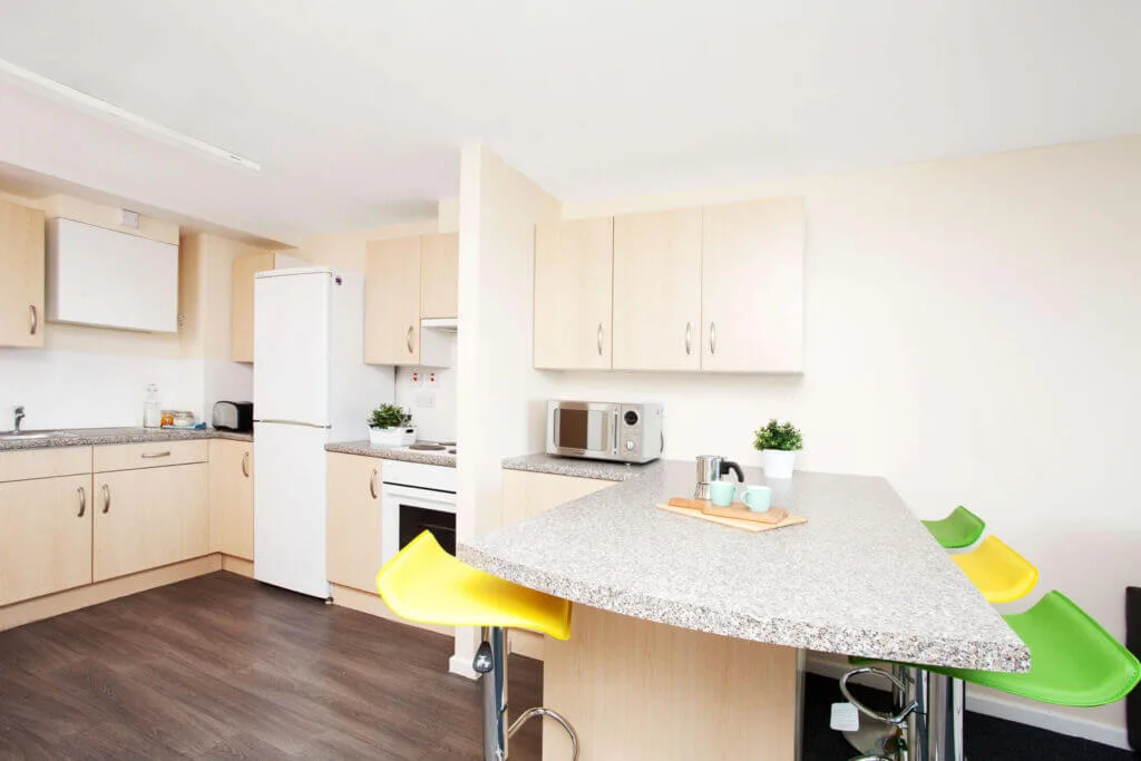 A bright and empty communal kitchen in one of Leeds' student accommodations, featuring a kitchen, an island, and green and yellow stools.