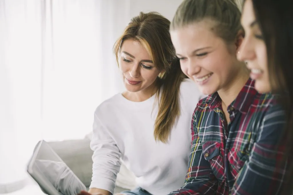 Group of young women smiling and looking at a laptop together for a student accommodation in Nottingham.