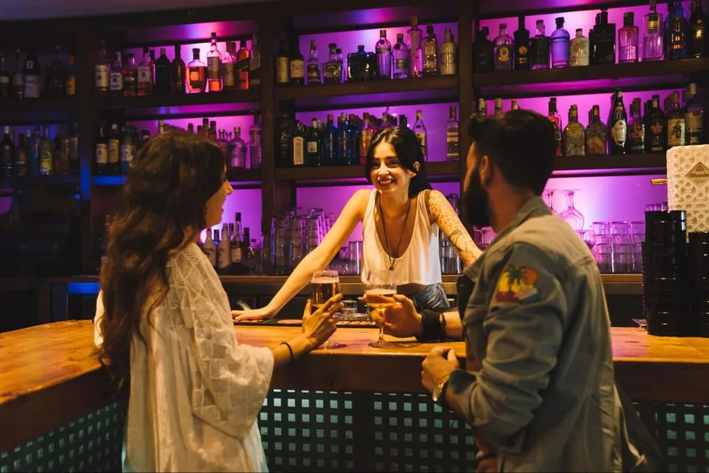 Students at a bar with shelves of bottles in the background, showcasing the social opportunities for students in Loughborough.