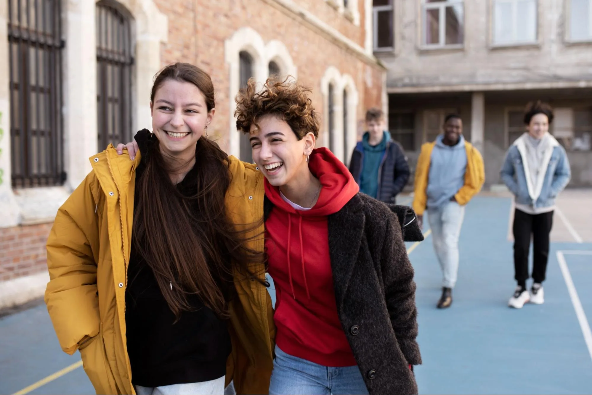 Group of cheerful students laughing and walking together outside a university building at student accommodations in Leicester