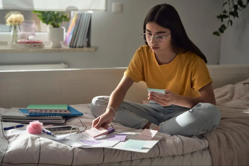 student organising study notes on her bed within a stylish and cosy room, showcasing the supportive environment of premium student accommodation at Exeter