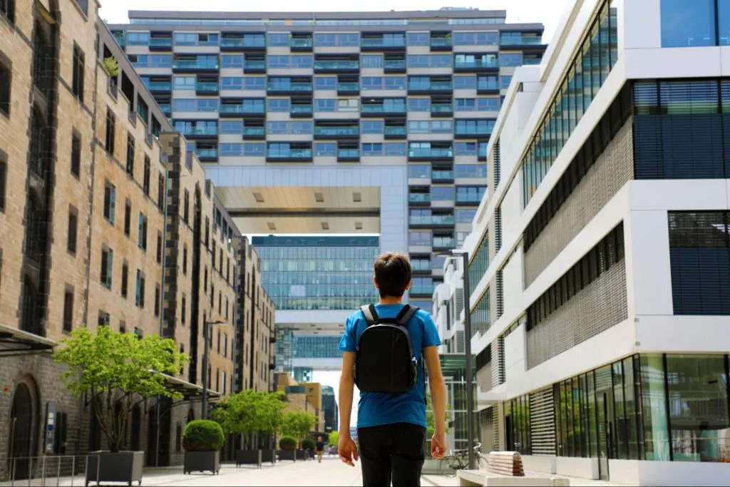A student with a backpack standing between modern city buildings