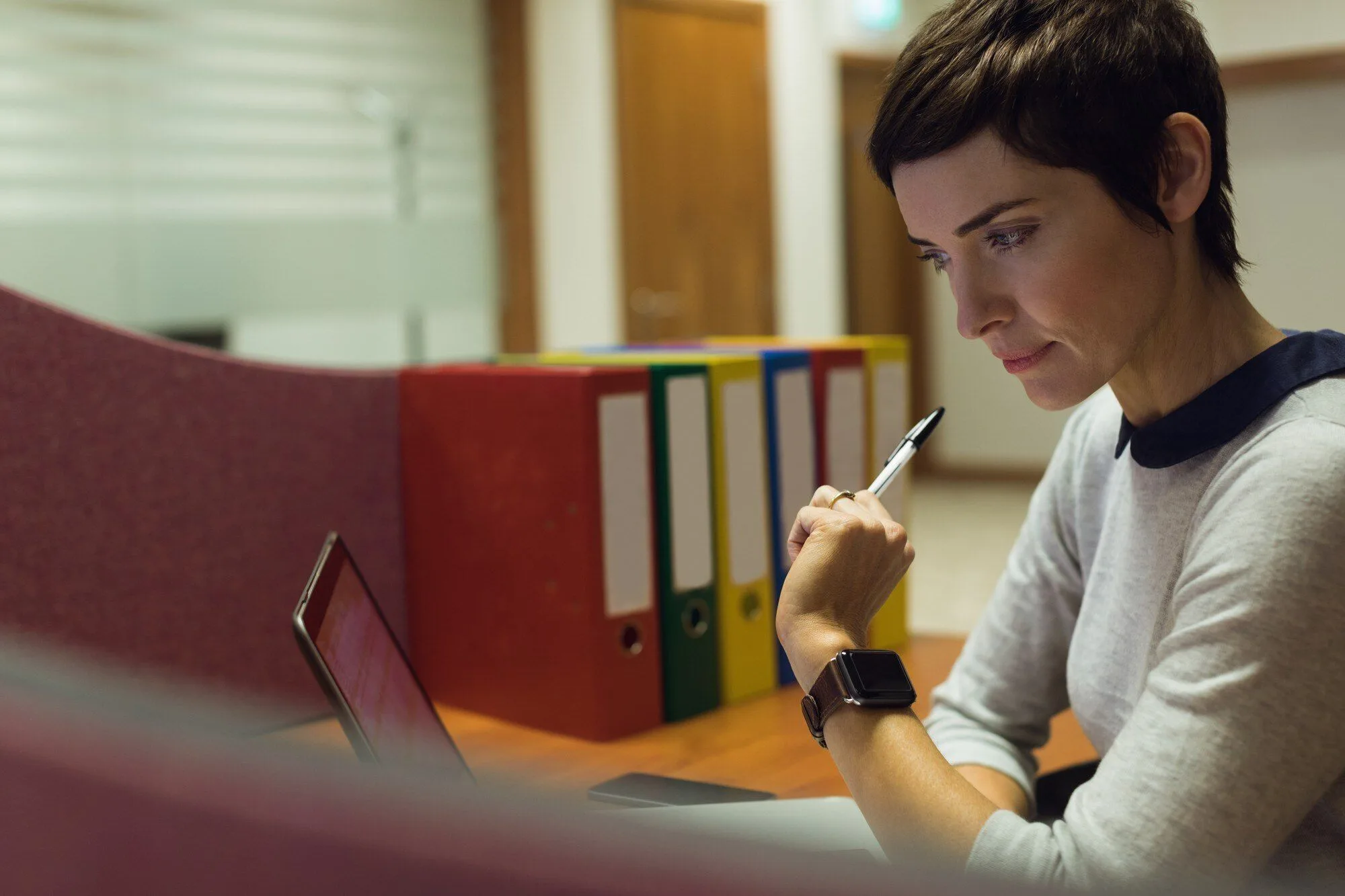 A student sitting at a desk with a pen and laptop, researching university course options during Clearing, colourful folders on the shelf behind her
