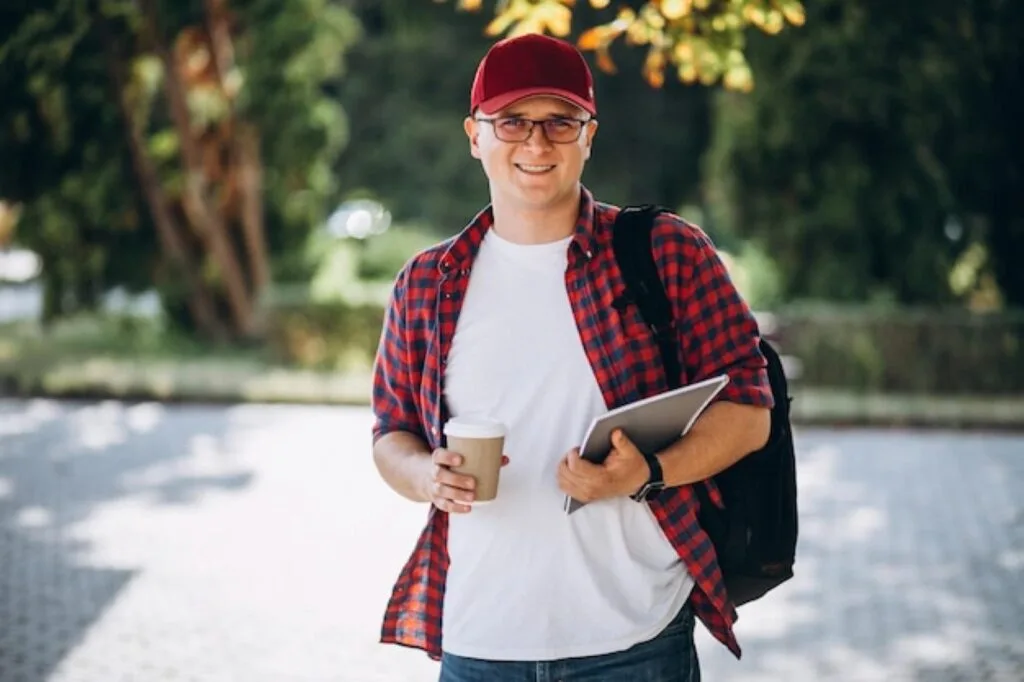 Student carrying a laptop and a coffee on campus in Leeds