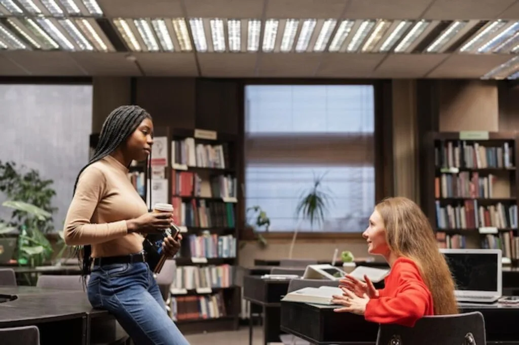 Two students studying together among library bookshelves