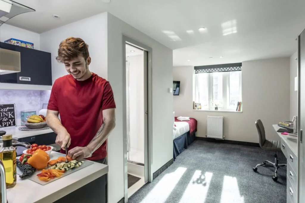 A student chopping vegetables in the kitchen of a studio at Study Inn Reynard House, Leicester, with the bed and desk beside the window