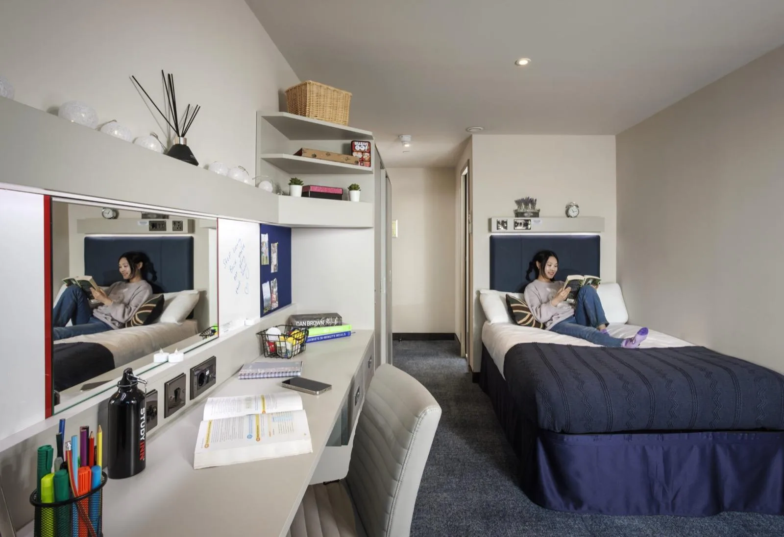 A student reading on her bed in an en-suite room at Study Inn Brotherton House, Leeds, with a desk, shelves and a pin board on the wall