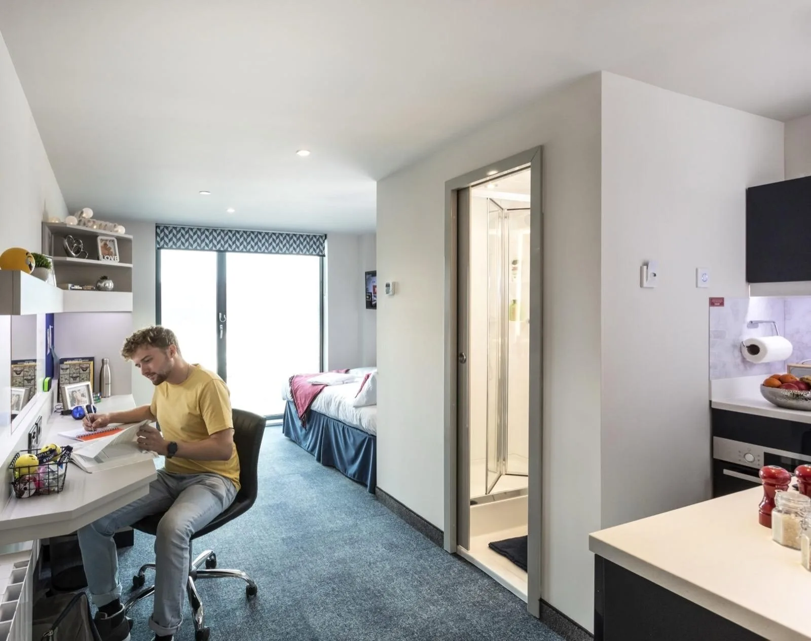 A student working at the desk in a studio at Study Inn Triumph House, Nottingham, with the bed and en-suite door behind him