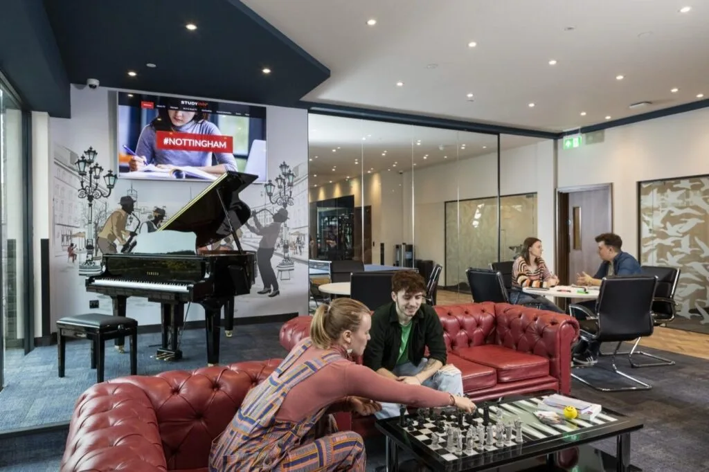 Students playing chess on red leather sofas beside a grand piano in the social area at Study Inn Triumph House, Nottingham