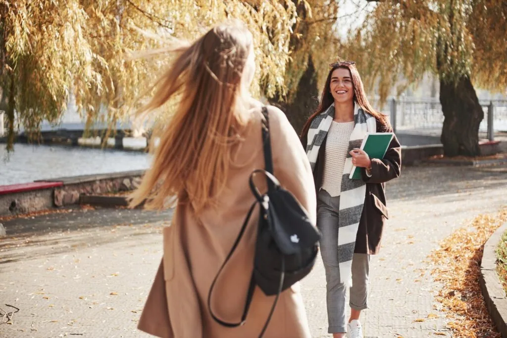Two friends with backpacks and folders meeting on a path in a park after lectures